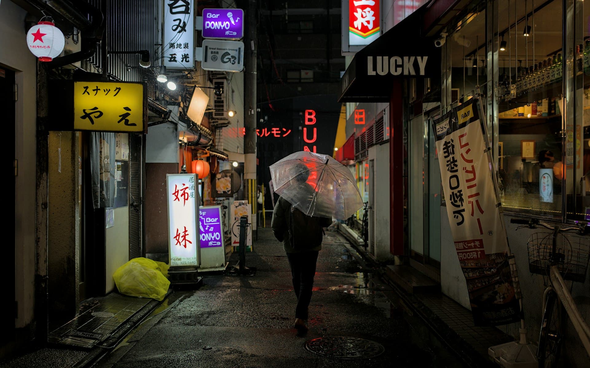 Person with umbrella walking down a rain-lit alley at night