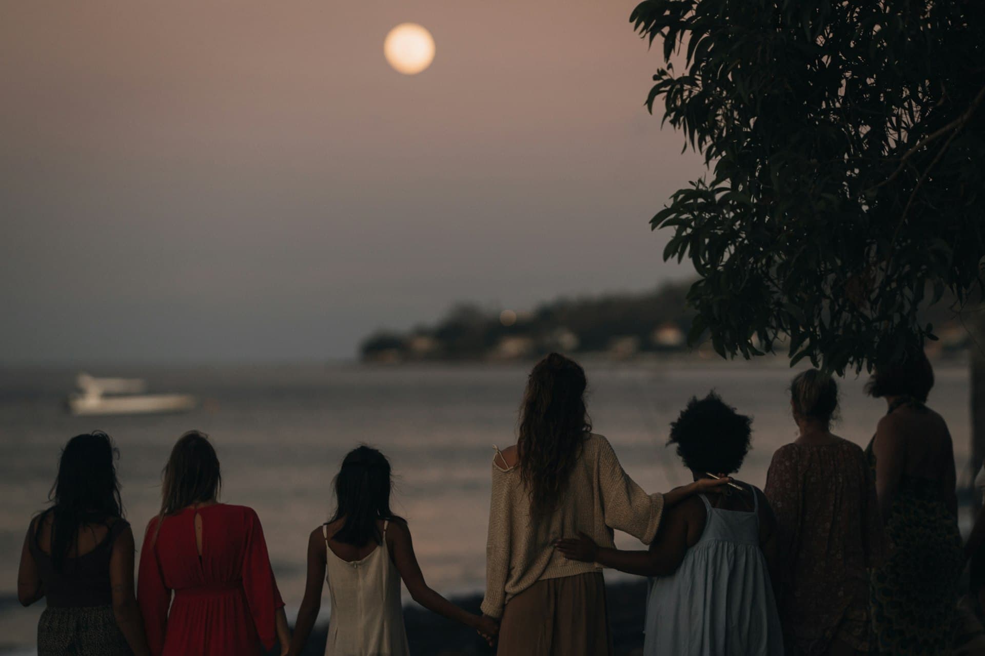 Group of women watching the moon over the ocean